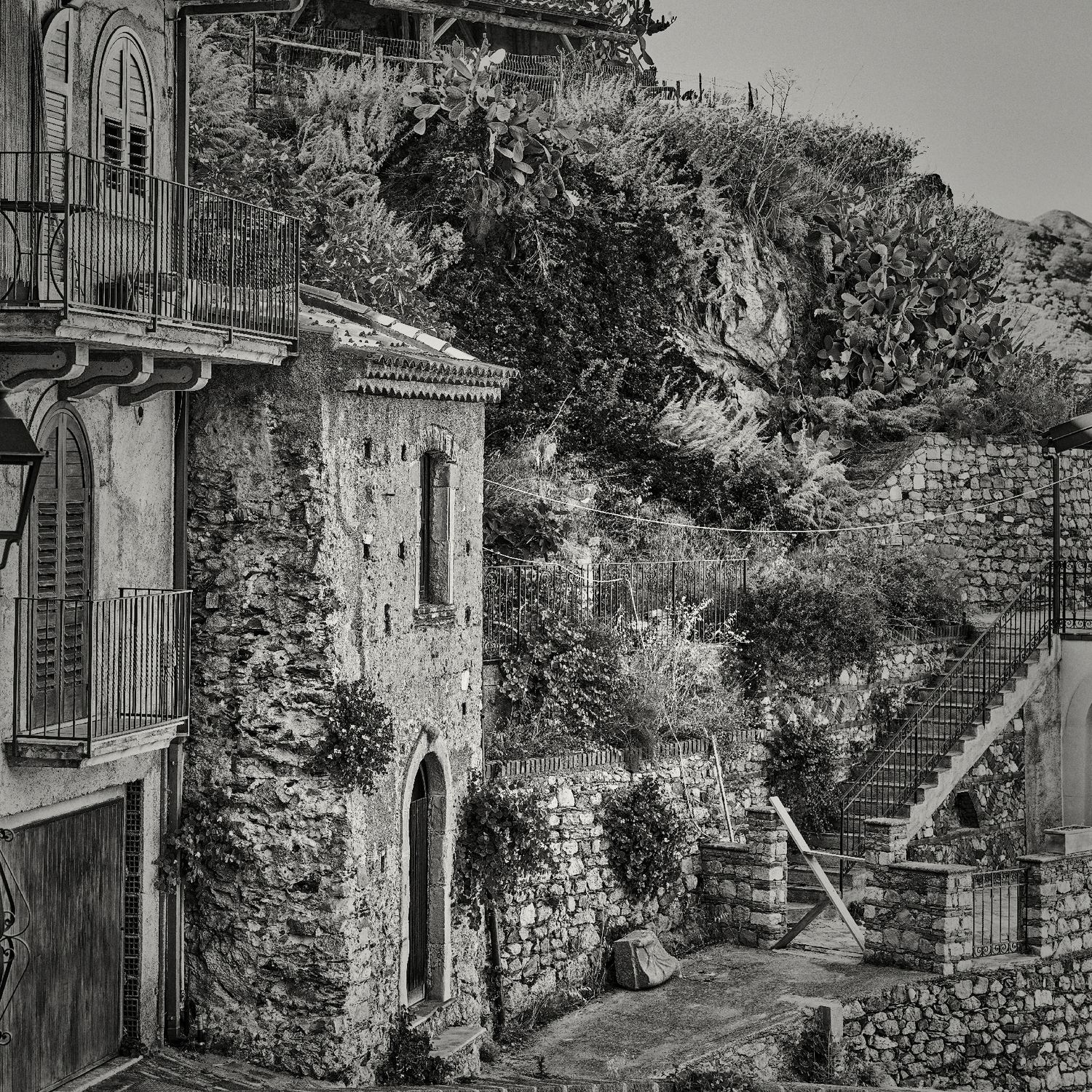 A series of black and white photographs showing stone buildings and pathways along a hillside with rustic architectural details.