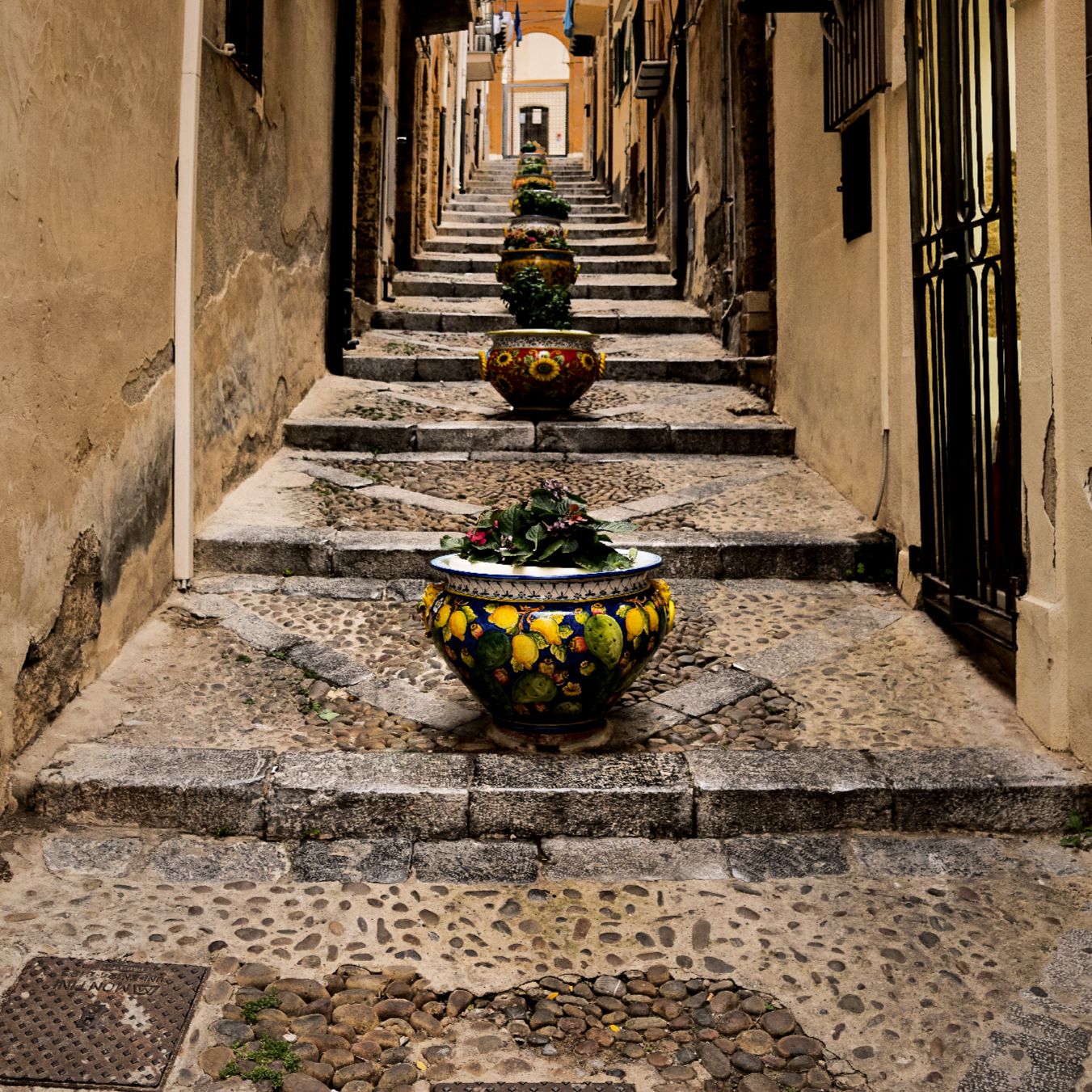 Narrow cobblestone alley with stone walls and decorative planters creating a charming Mediterranean atmosphere.