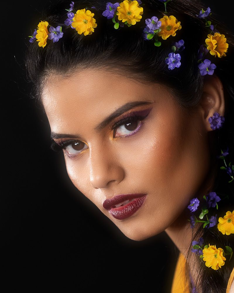 Artistic beauty portrait with purple and yellow flowers against dark background creating ethereal floral crown effect.
