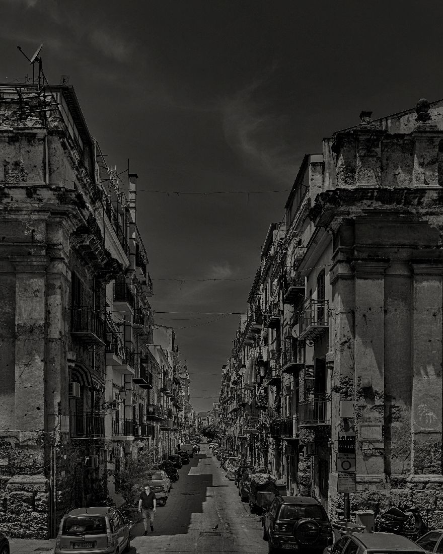 Dramatic black and white cityscape showing war-damaged buildings along a narrow street in ruins.