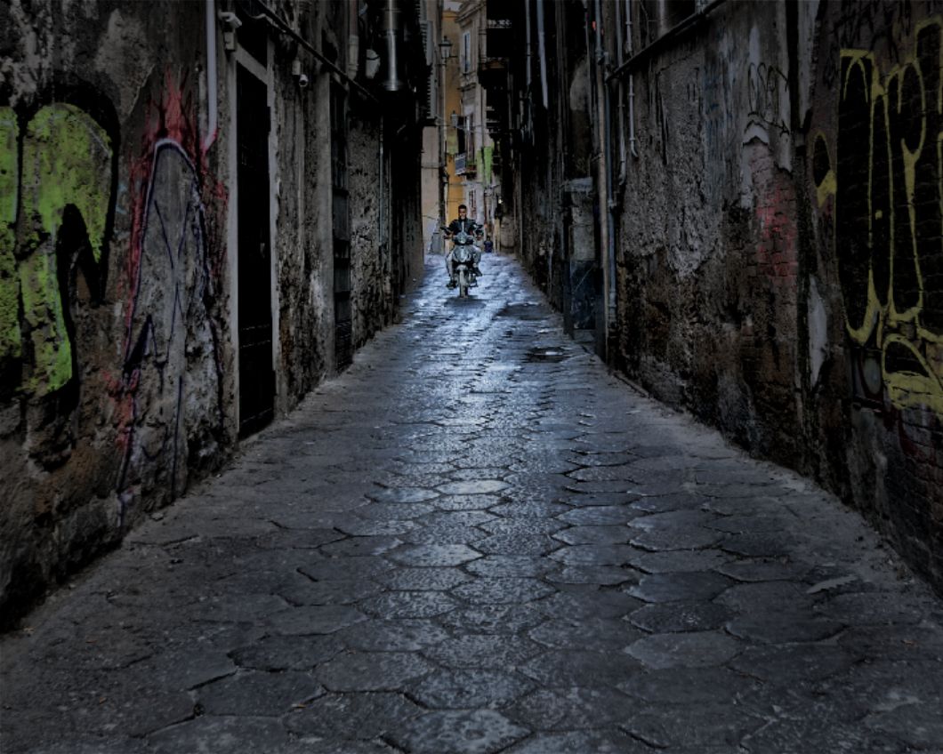 Dark narrow alley with stone walls and wet cobblestones reflecting dim light in an old European city.