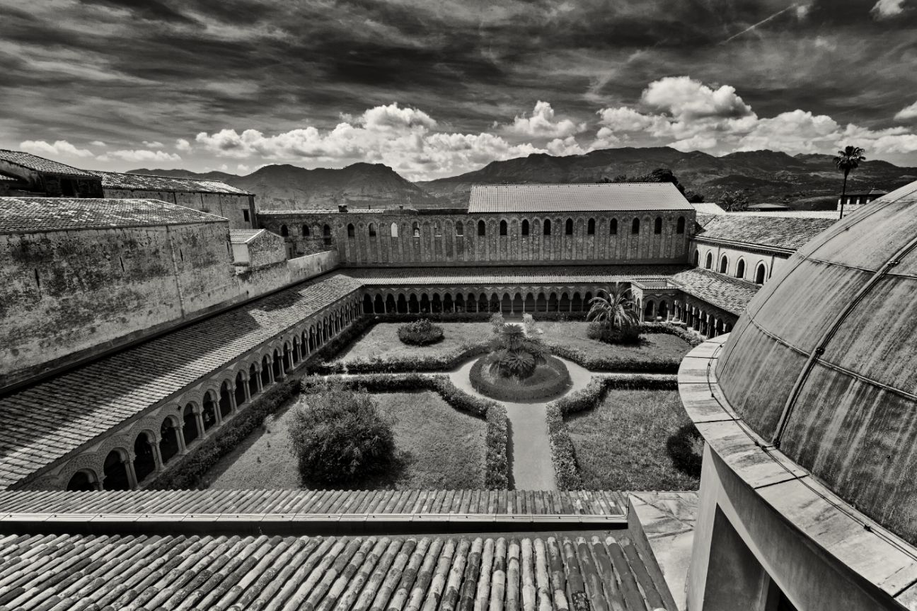 Aerial view of a monastery courtyard with geometric gardens and architectural features under dramatic cloudy skies.
Horvath-Photography