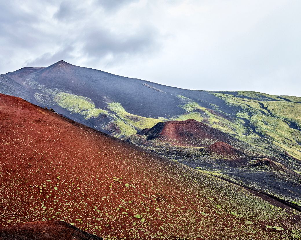 Panoramic view of Mount Etna's volcanic landscape showing red cinder cones and green slopes in Sicily.