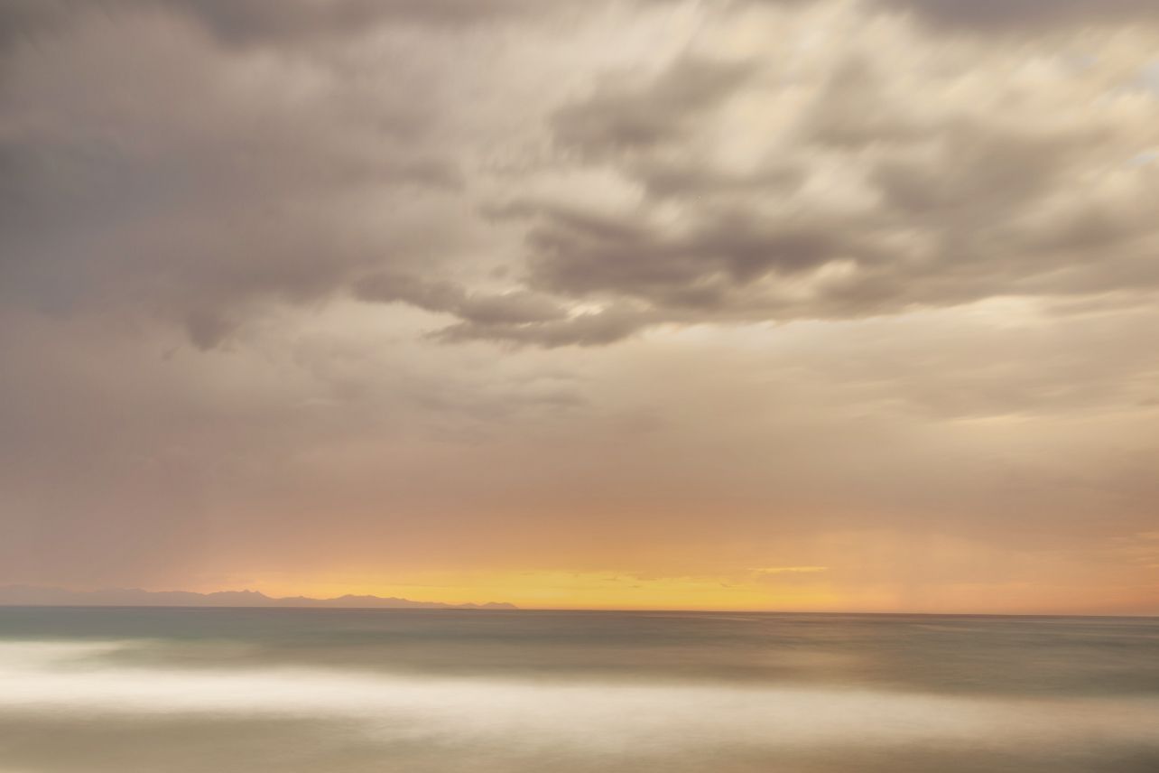 Dramatic sunset sky over the ocean with dark clouds and golden horizon.