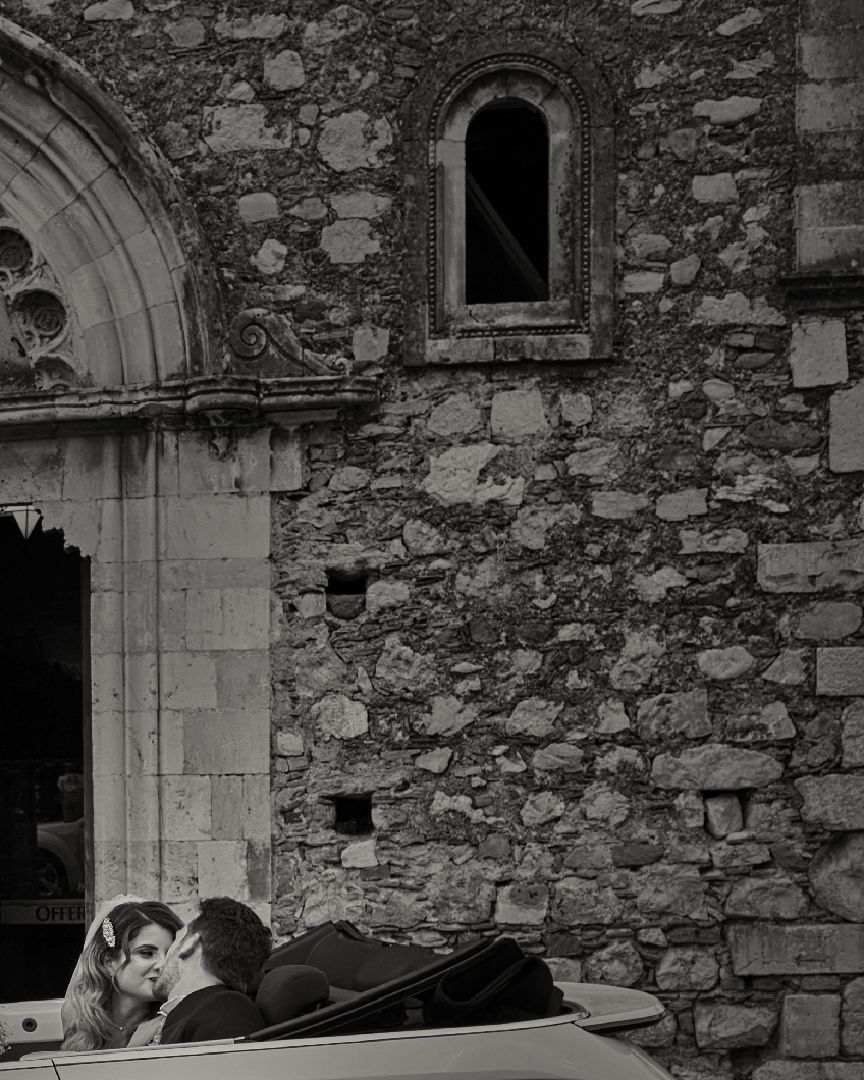 A couple shares an intimate moment while resting on stone steps outside an old church with rustic stone walls.
Horvath-Photography-