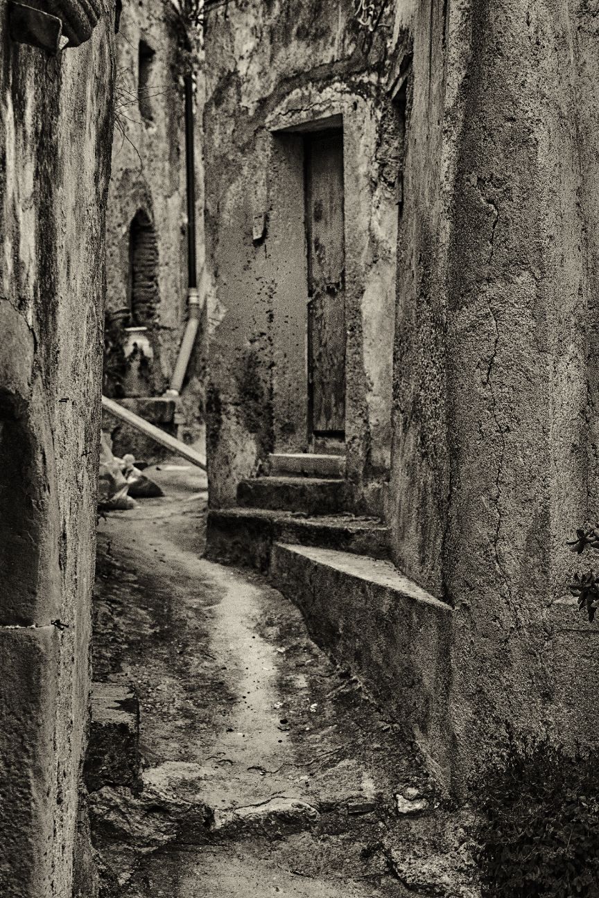 A narrow, winding alleyway with weathered stone walls and steps leads through an old Mediterranean village
Horvath-Photography-Sam-Sciarrino