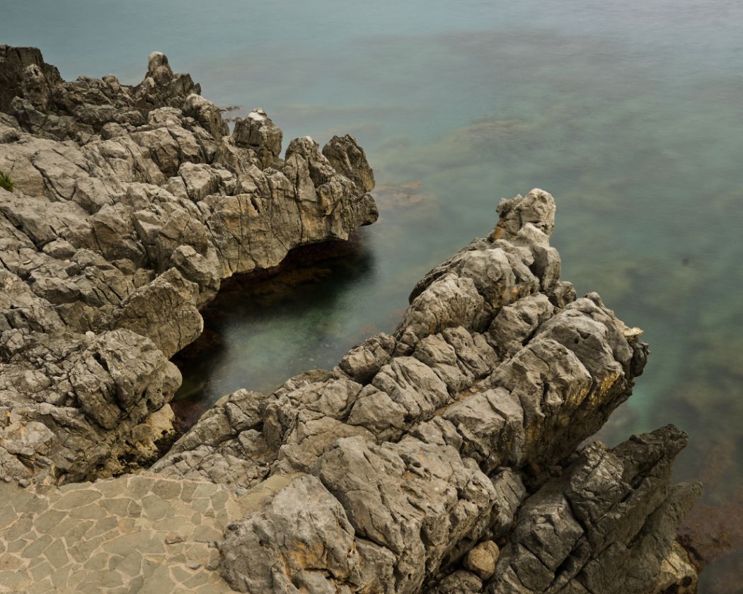 A panoramic sequence showing rocky coastal formations jutting into turquoise Mediterranean waters on a sunny day.