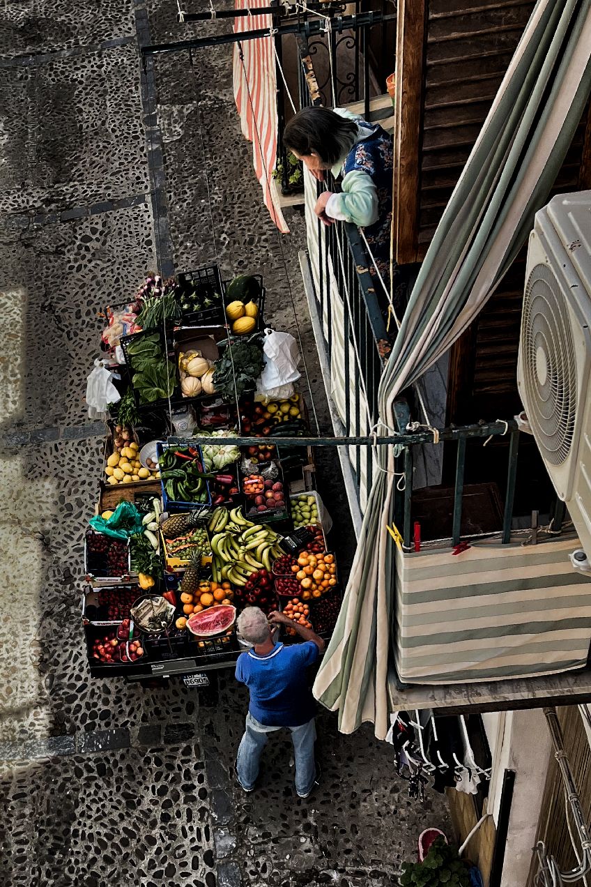 People browse fresh produce and goods at an outdoor market stall with striped awnings and stone pillars.
Horvath-Photography-Sam-Sciarrino