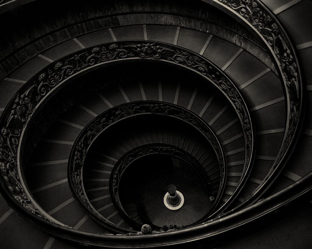 Aerial view of the iconic spiral staircase at the Vatican Museums with dramatic black and white lighting.