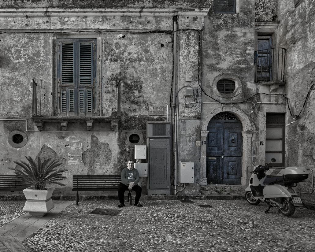 A series of weathered stone buildings with rustic blue doors and shutters along an old Mediterranean courtyard.
Horvath-Photography