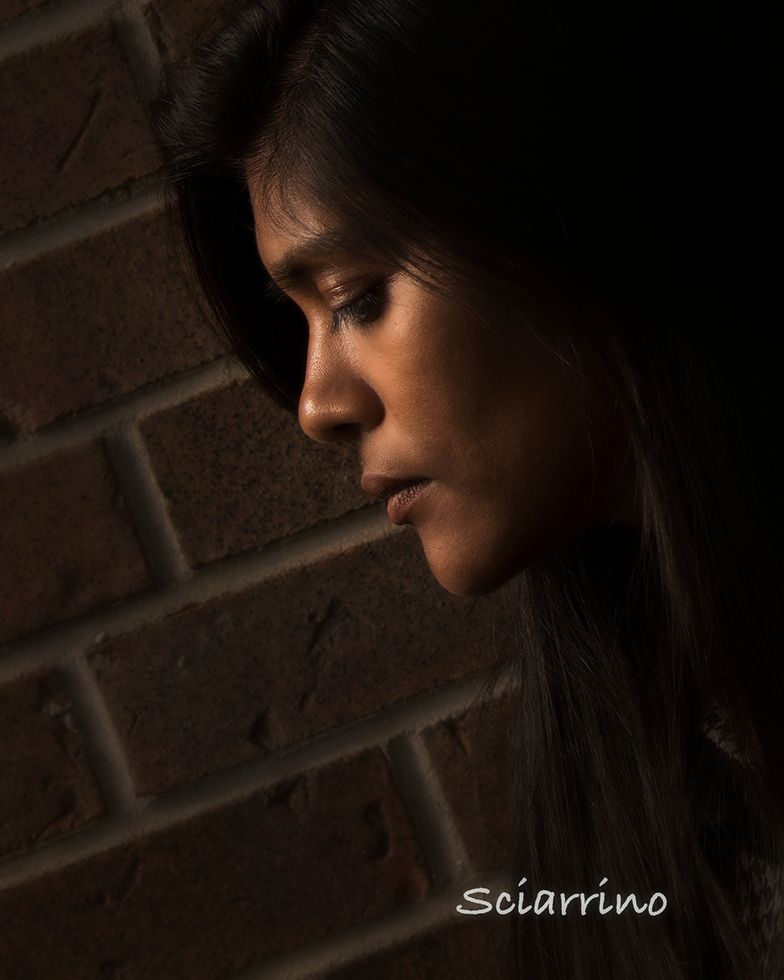 A dramatic side profile silhouette in low key lighting against a dark brick wall creates a moody artistic portrait.
