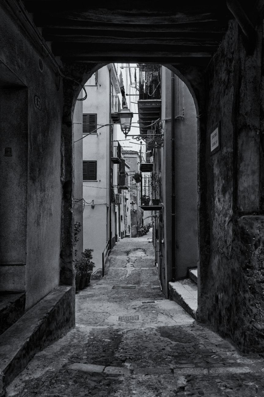 A series of black and white photographs showing narrow, shadowy alleyways with stone walls and archways in an old town.
Horvath-Photography-