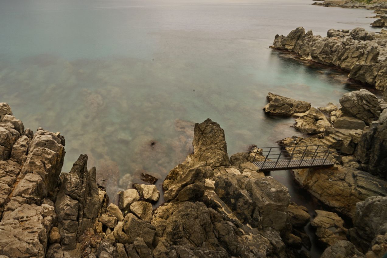 Rocky coastline with jagged formations and turquoise waters stretching along the Mediterranean shore in golden sunlight.
Horvath-Photography