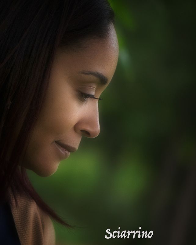 Portrait in profile against blurred green background with dramatic lighting and soft shadows.