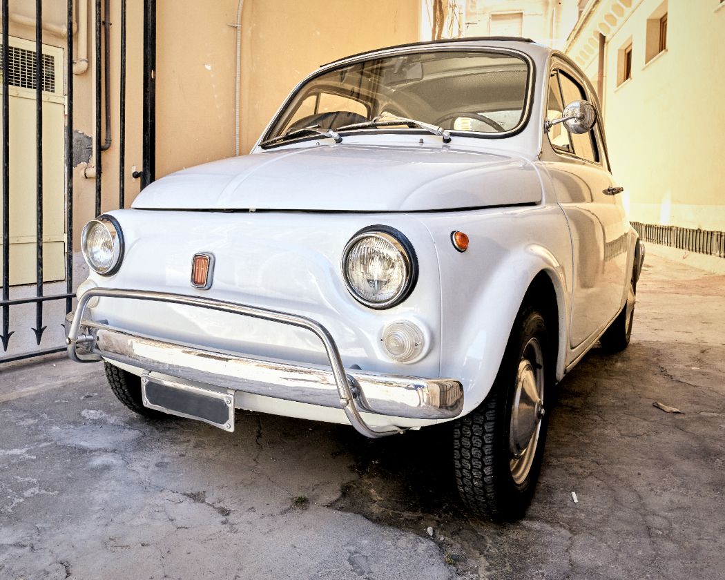 Row of vintage white Fiat 500 cars parked along a narrow Italian street.