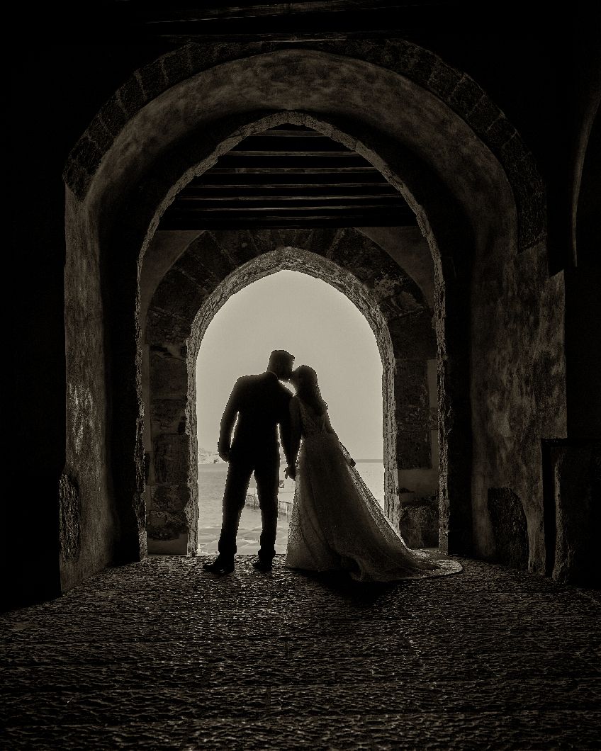 Silhouetted figures stand in dramatic archway tunnel creating romantic shadows and light contrast.Horvath-Photography-Sam-Sciarrino