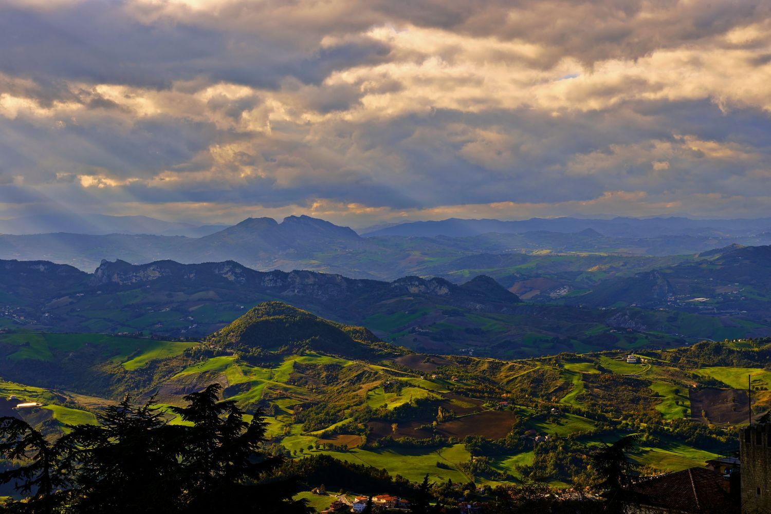 Dramatic sunset over green rolling hills and mountains with sunbeams breaking through cloudy sky in rural landscape.
Horvath-Photography-