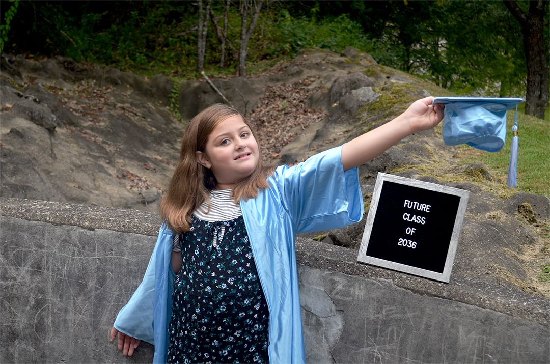 Child in blue cap and gown posing by future Class of 2040 sign during Mini Grad session