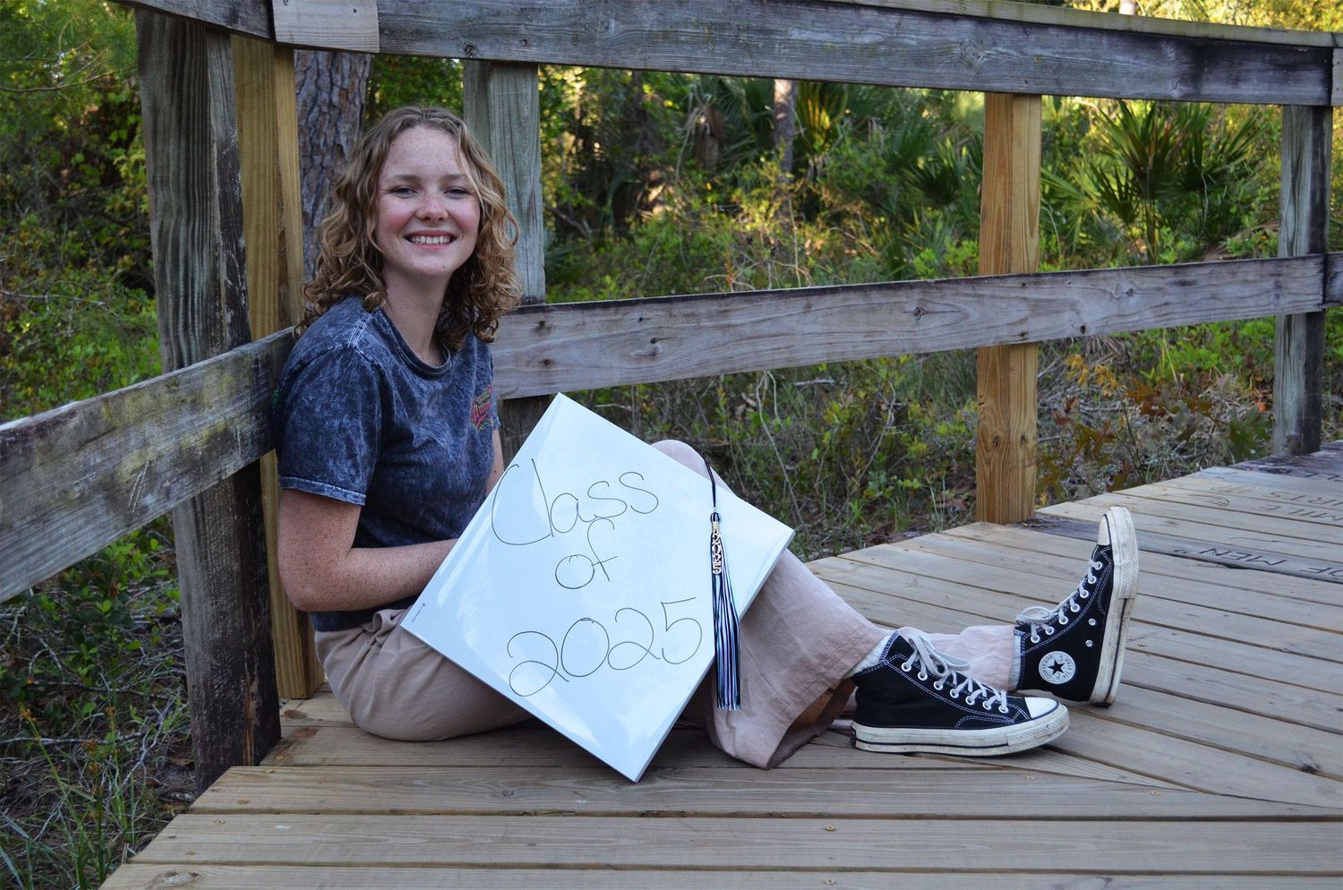 High school senior sitting on bridge holding Class of 2025 sign during graduation portrait session in Brevard County, Florida