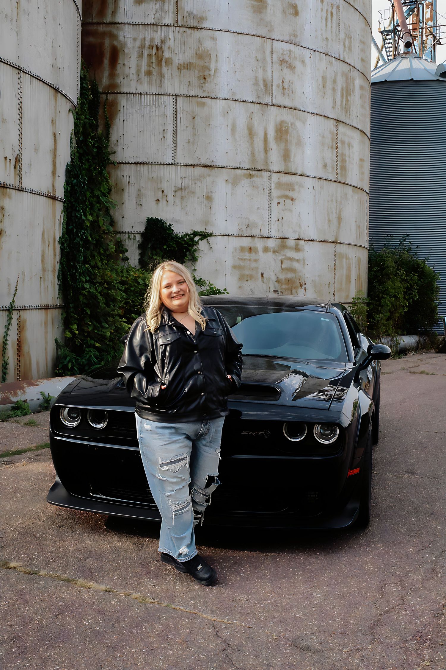 Black sports car parked near industrial storage tanks in an urban setting.