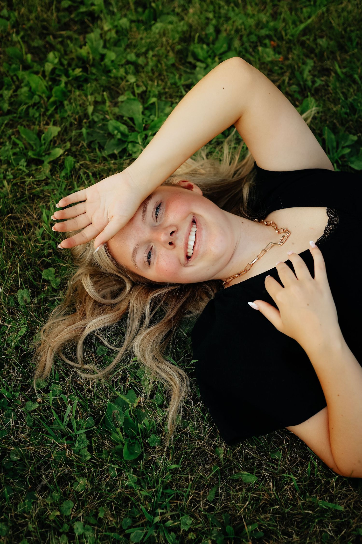 A woman in black lying on grass smiling at the camera.