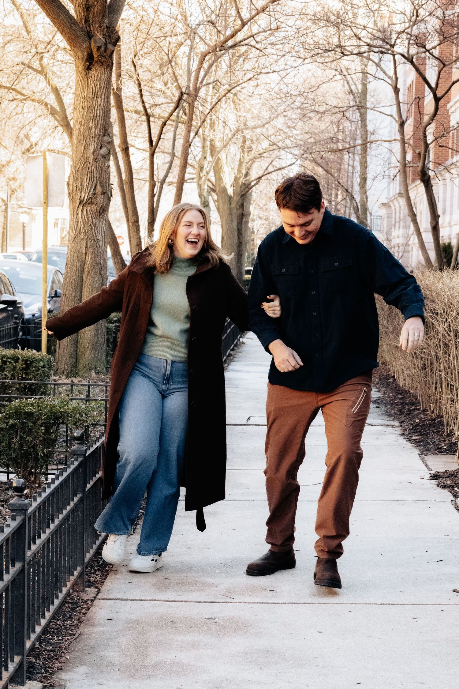 Playful couple walking and laughing together on a snowy winter sidewalk.