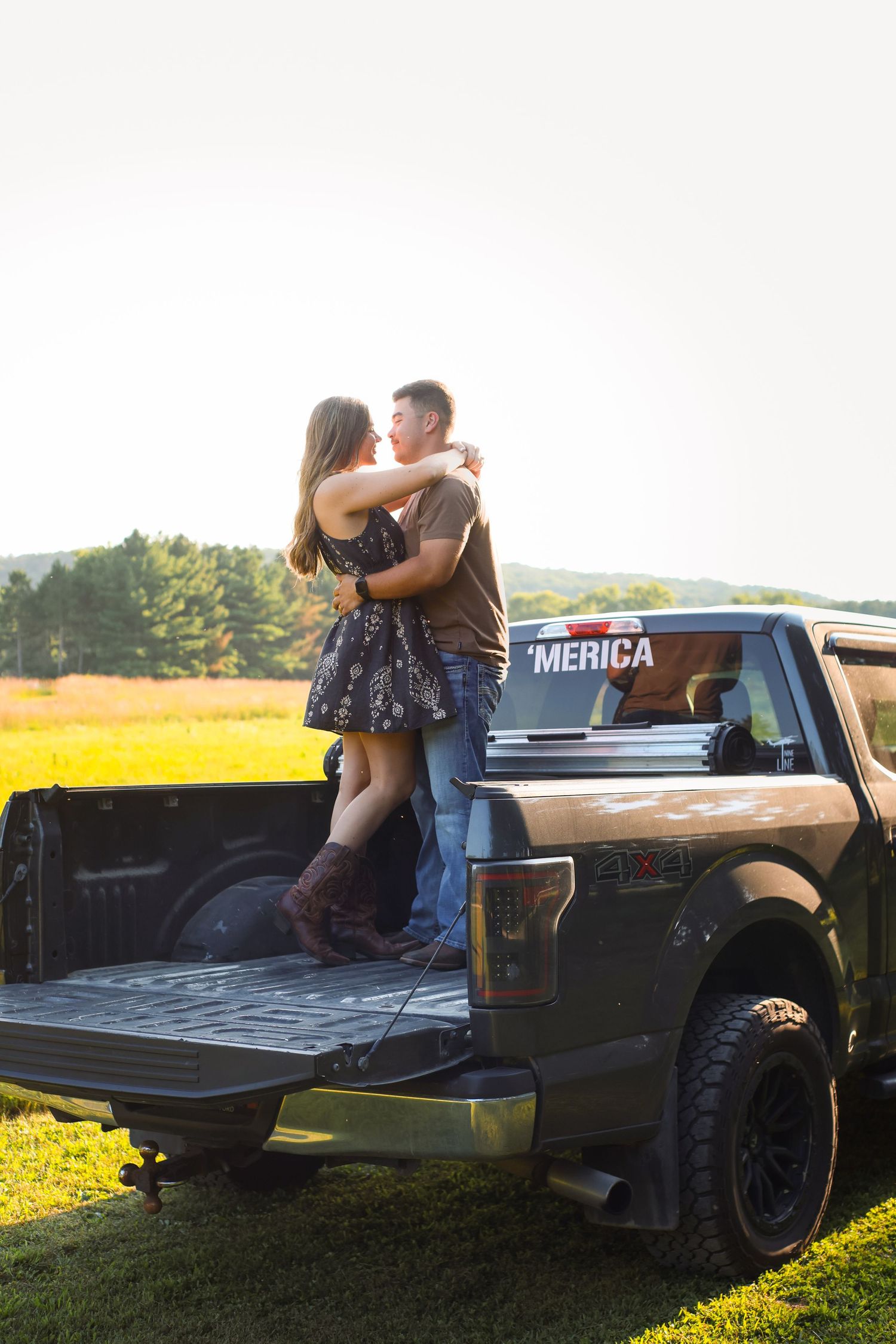 Romantic couple sitting in the bed of a pickup truck at sunset surrounded by golden fields.
