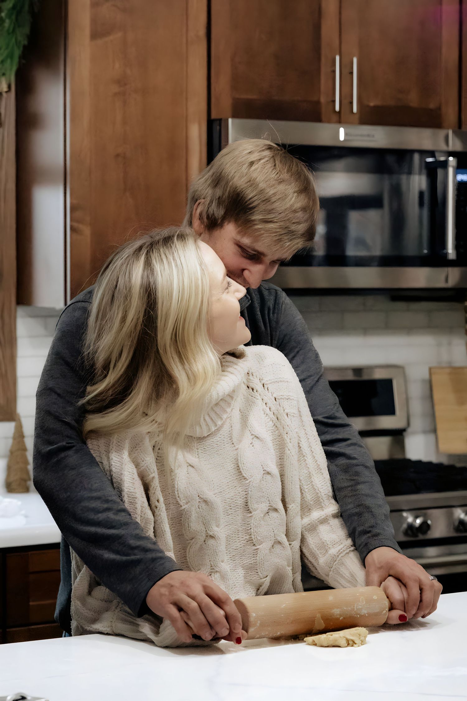 Couple baking together in modern kitchen while rolling dough on white counter.