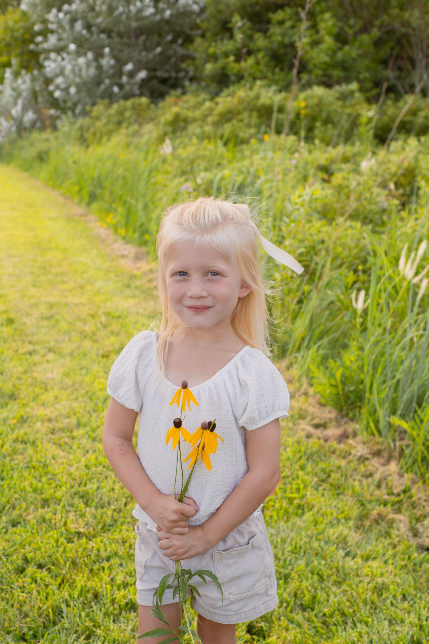 A child in a white dress holds yellow flowers in a summer garden.