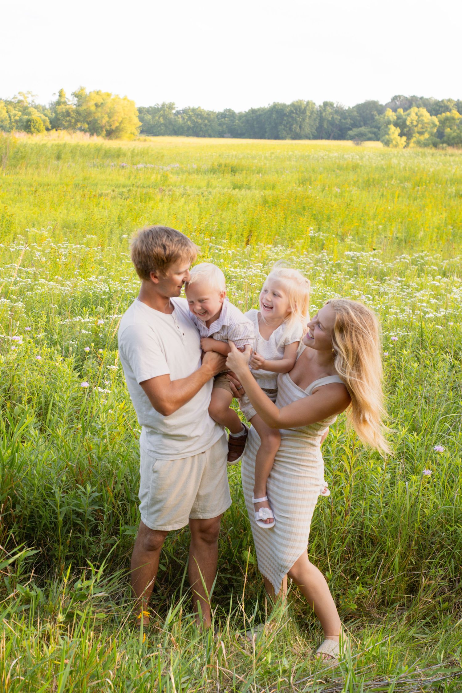 Family enjoying a playful moment together in a sunny meadow filled with wildflowers.