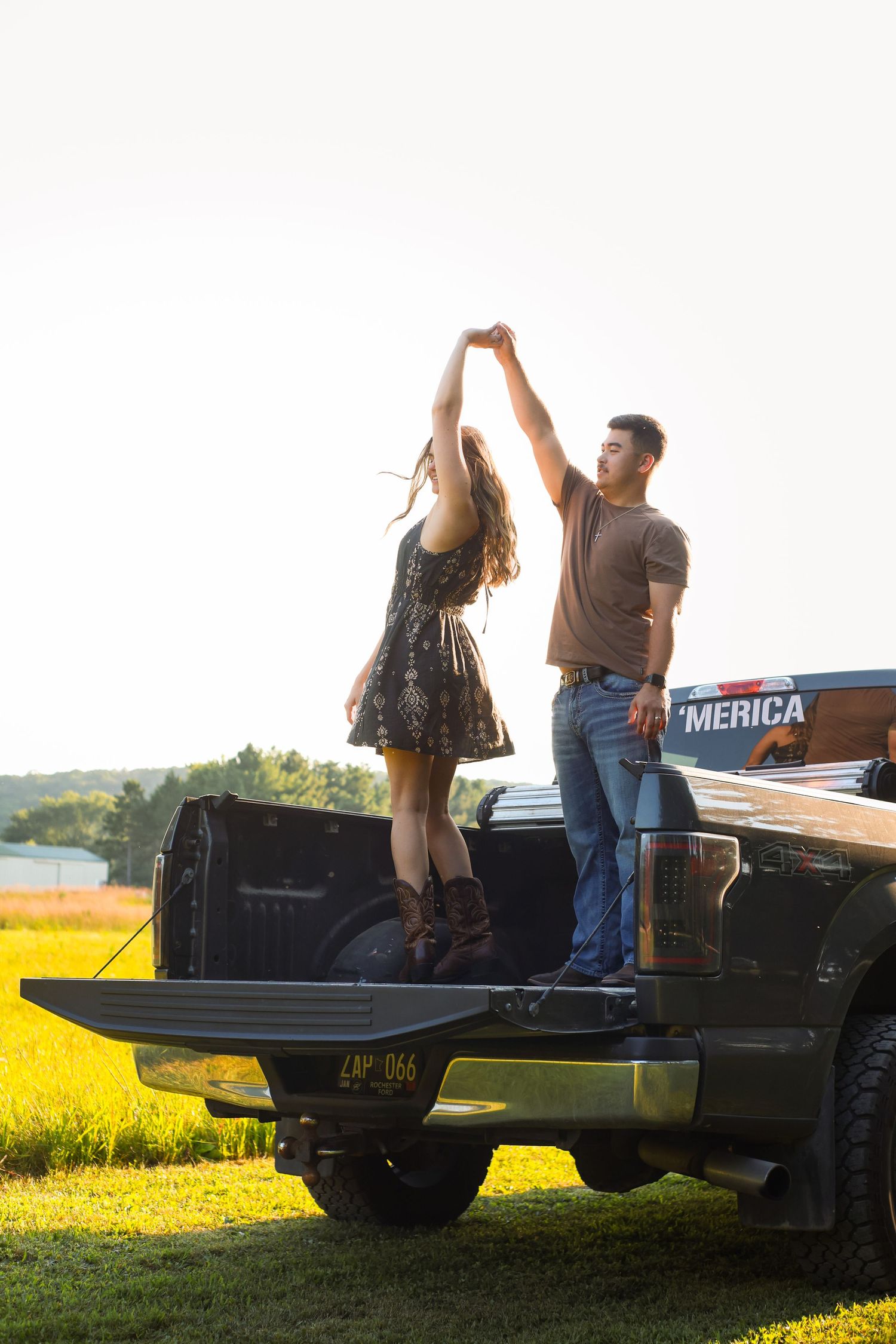 A couple dancing on the back of a pickup truck at sunset with yellow wildflowers in the background.