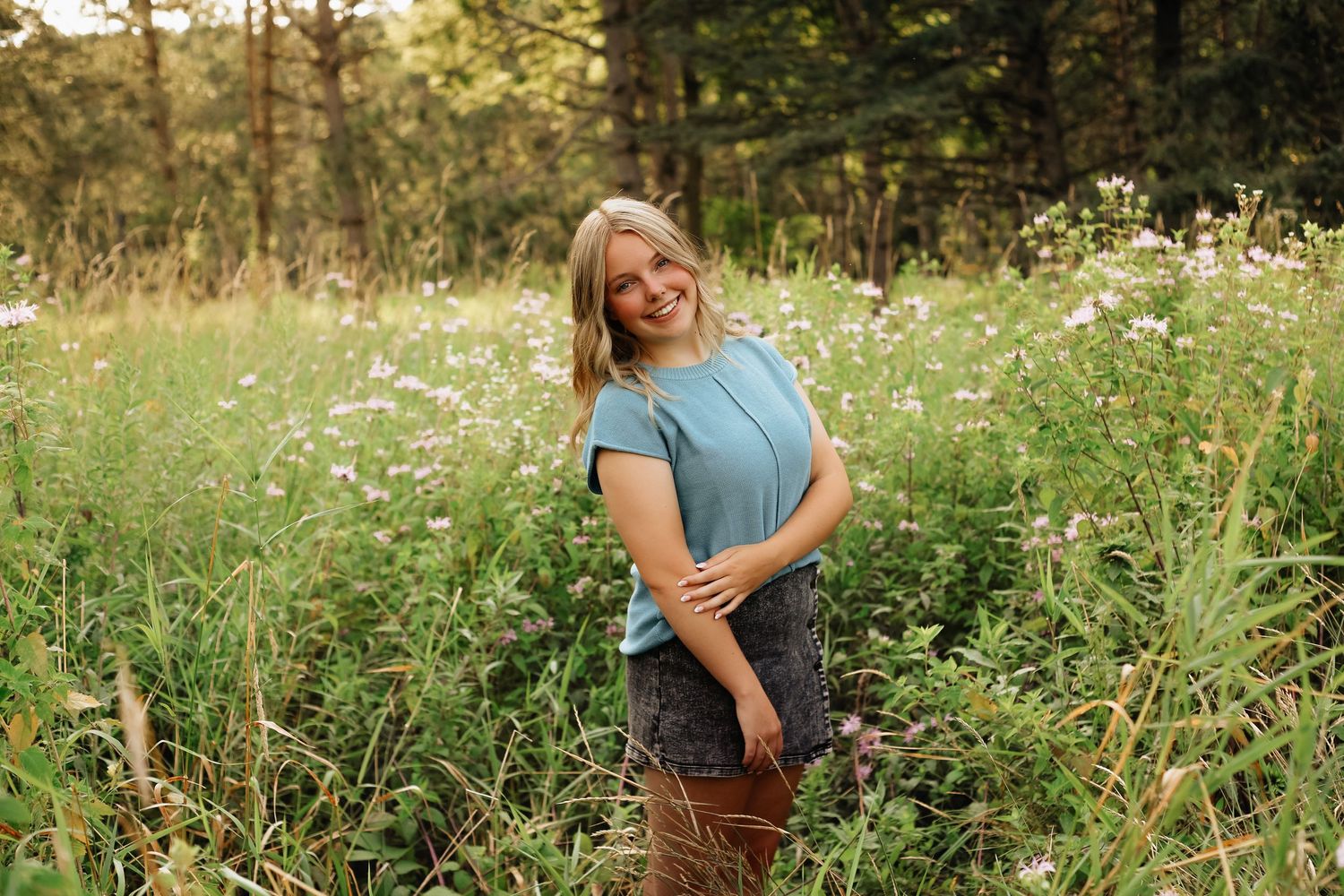 Woman in blue top posing in wildflower meadow during golden hour.
