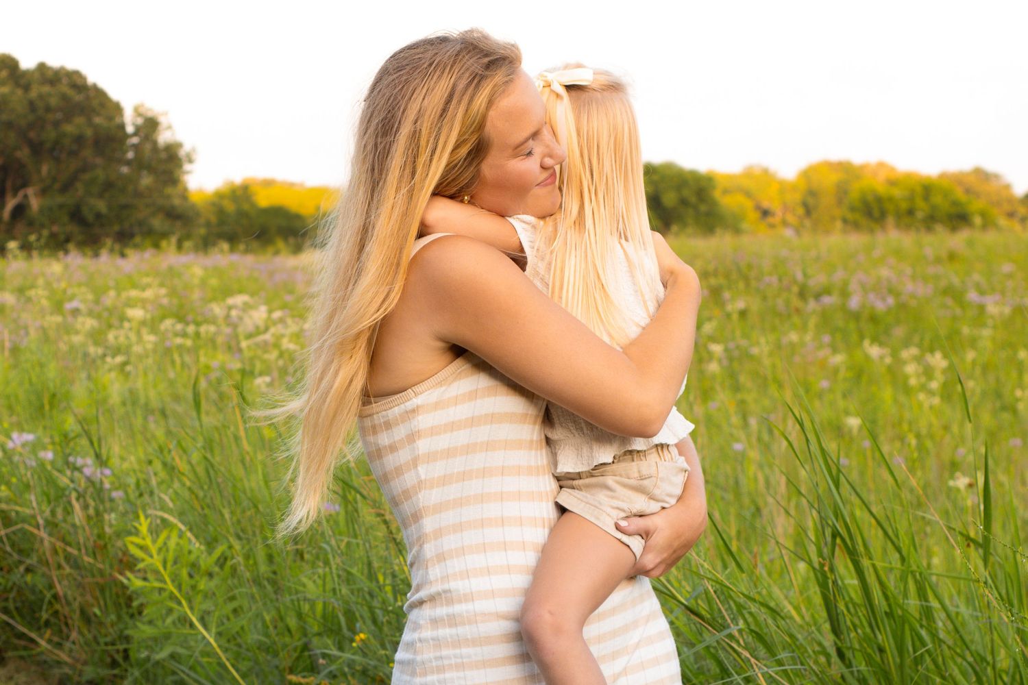 A tender embrace captured in a sunlit meadow with tall grass and wildflowers.
