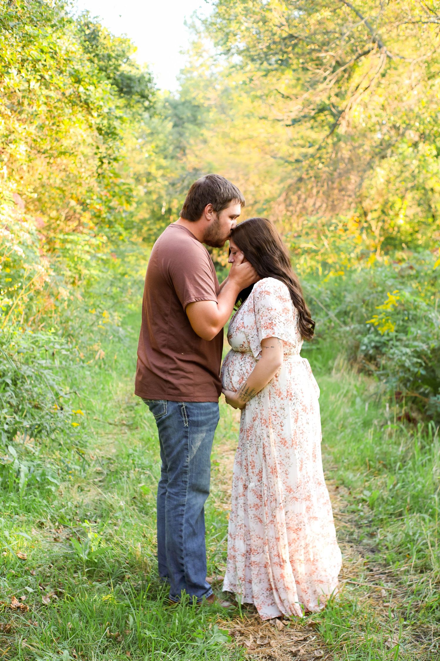 Romantic outdoor maternity photoshoot in a sunlit wooded path.