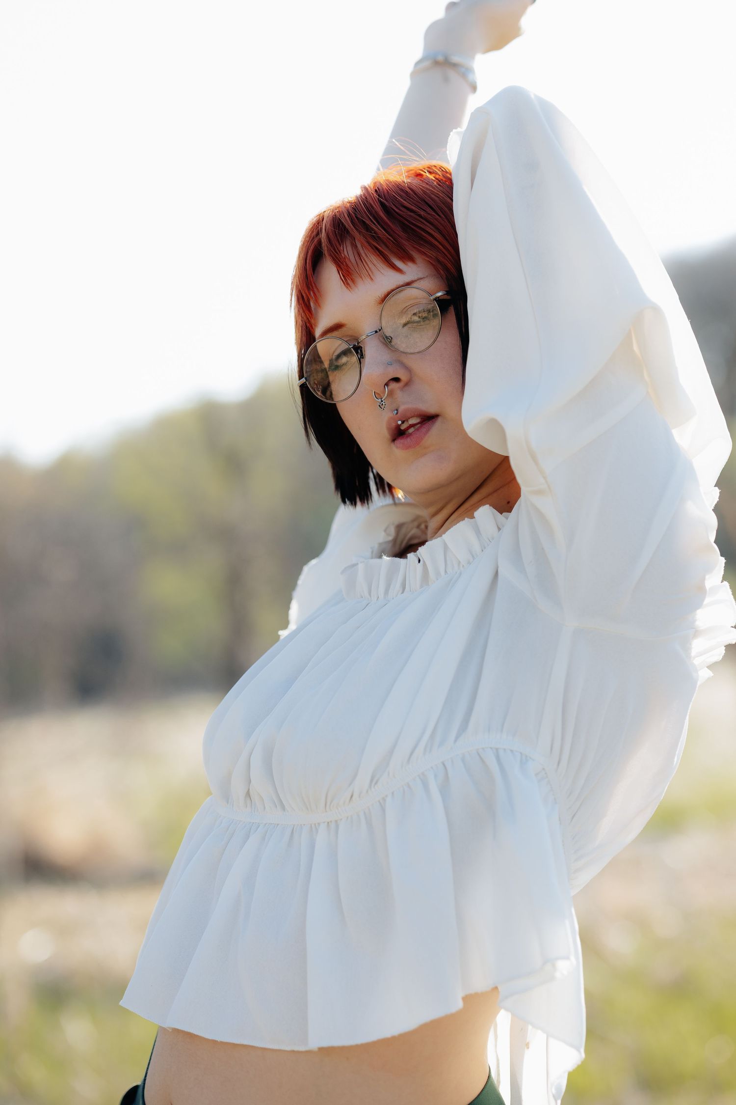 Person in white ruffled top poses gracefully in natural sunlight.