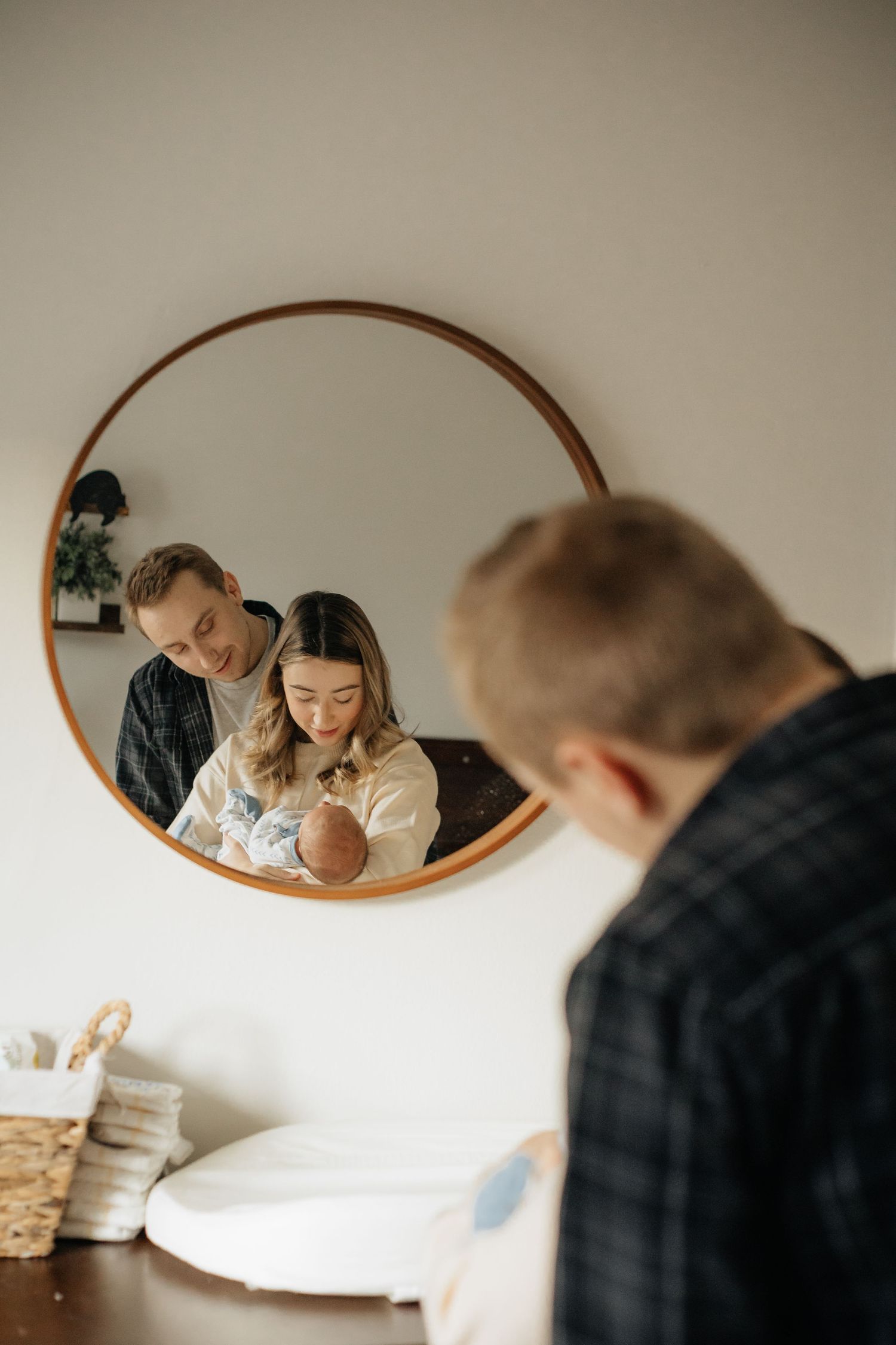 Family moment reflected in round wooden mirror while holding baby.