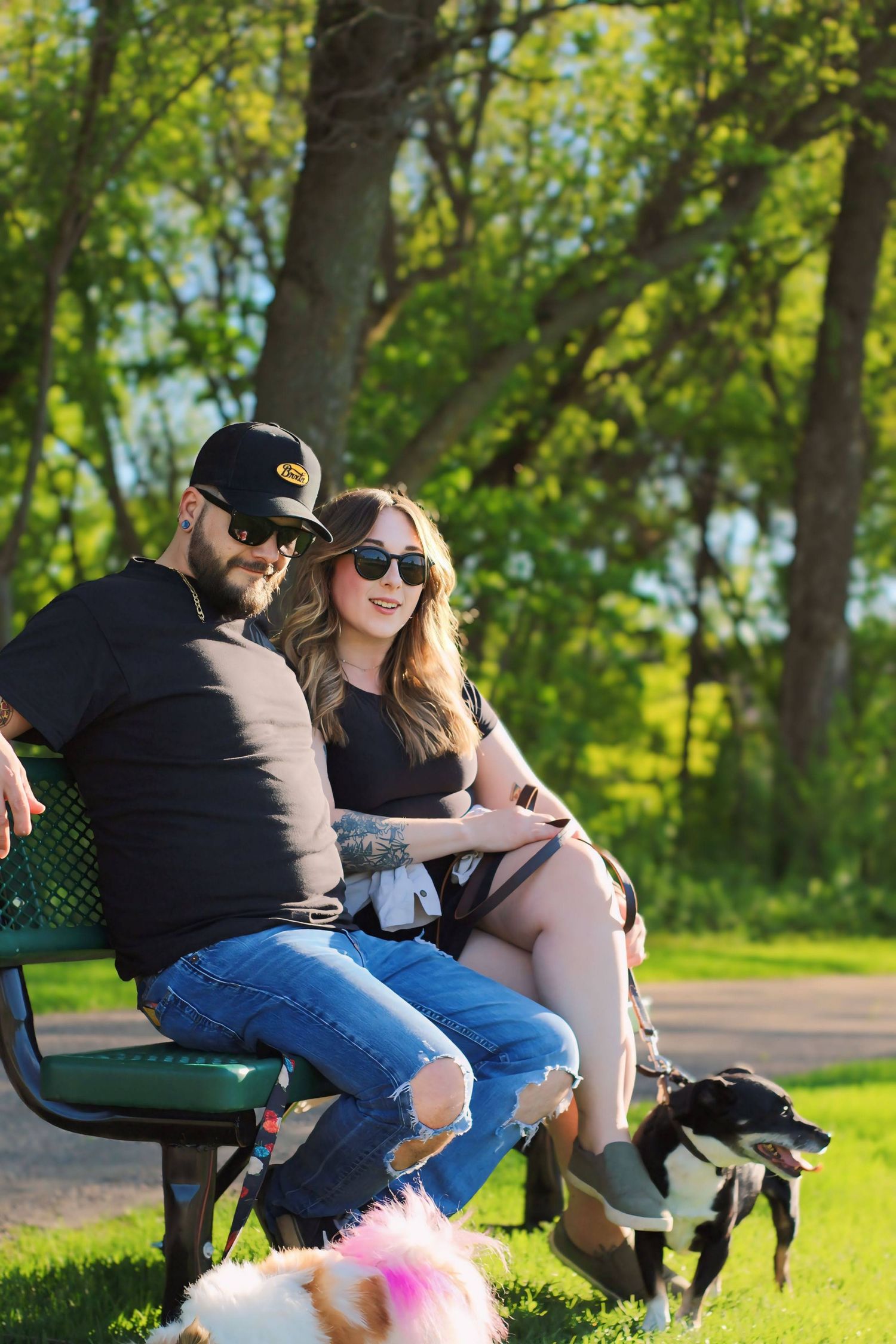 People relaxing on park bench surrounded by green trees on sunny day.