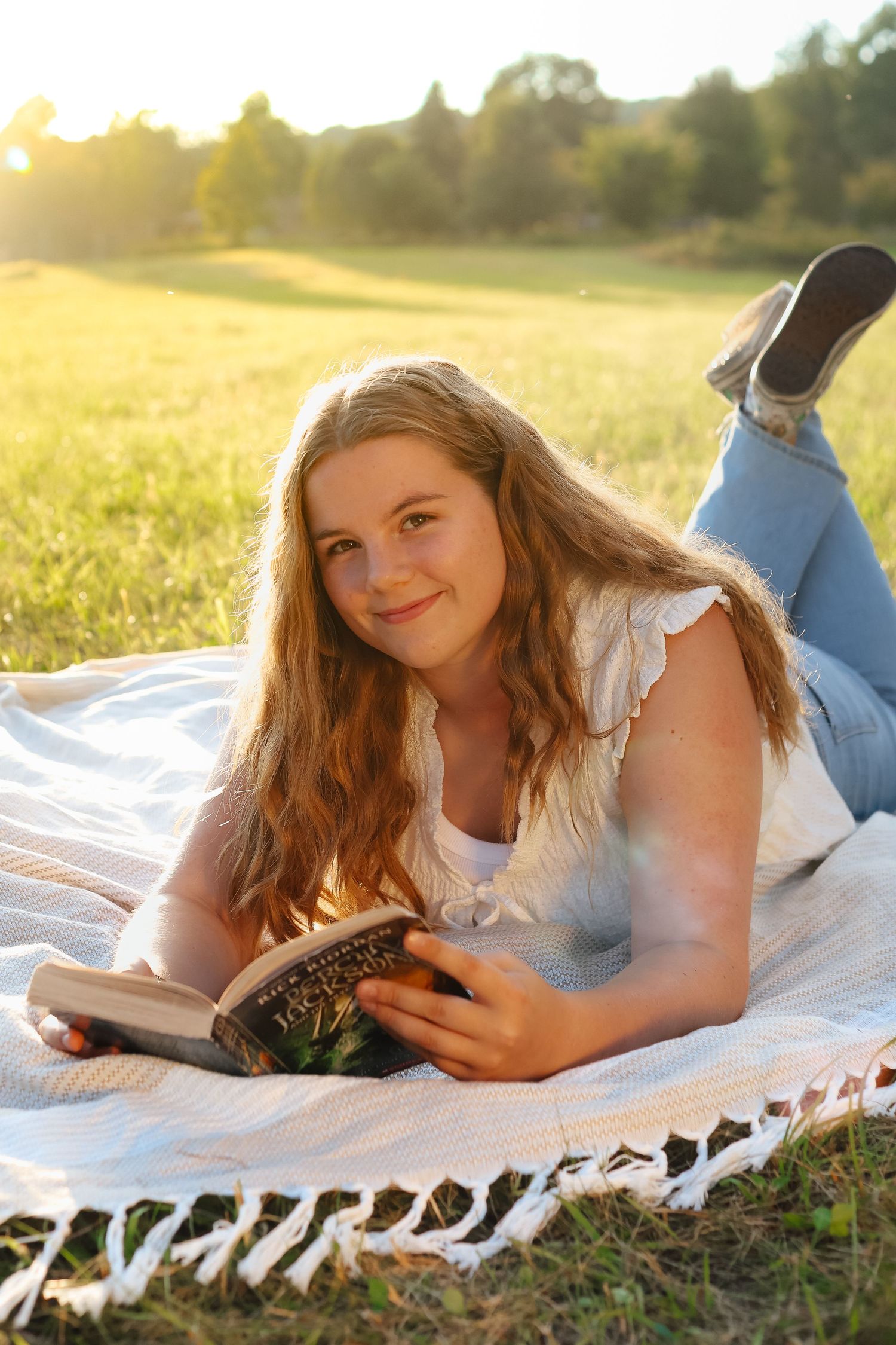 Someone reading a book while relaxing on a white blanket in a sunny field at golden hour.