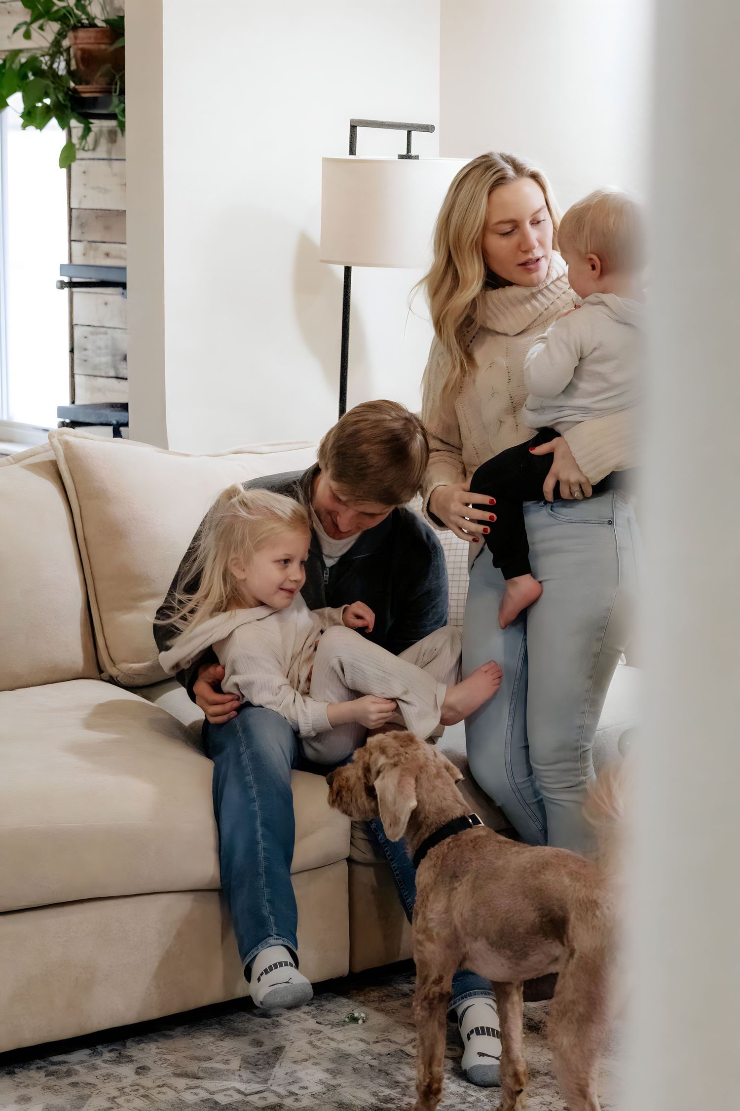 Family relaxing on white couch with their dog in bright living room.