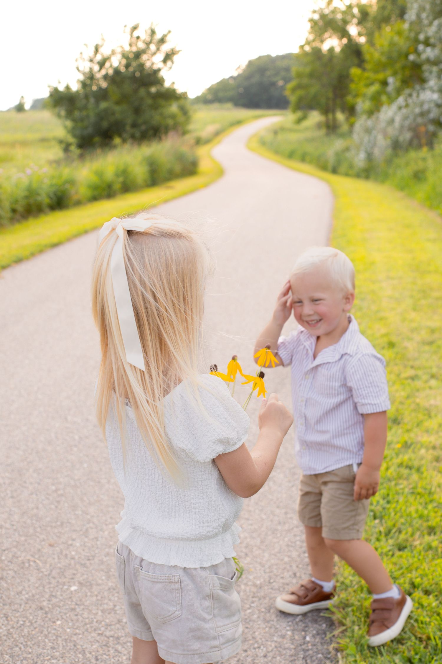 Children share a sweet moment with flowers on a winding country path.