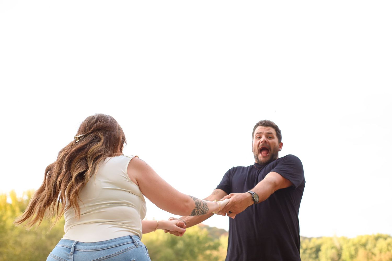 A couple spins together in a golden sunlit field during sunset, creating a romantic and joyful moment.