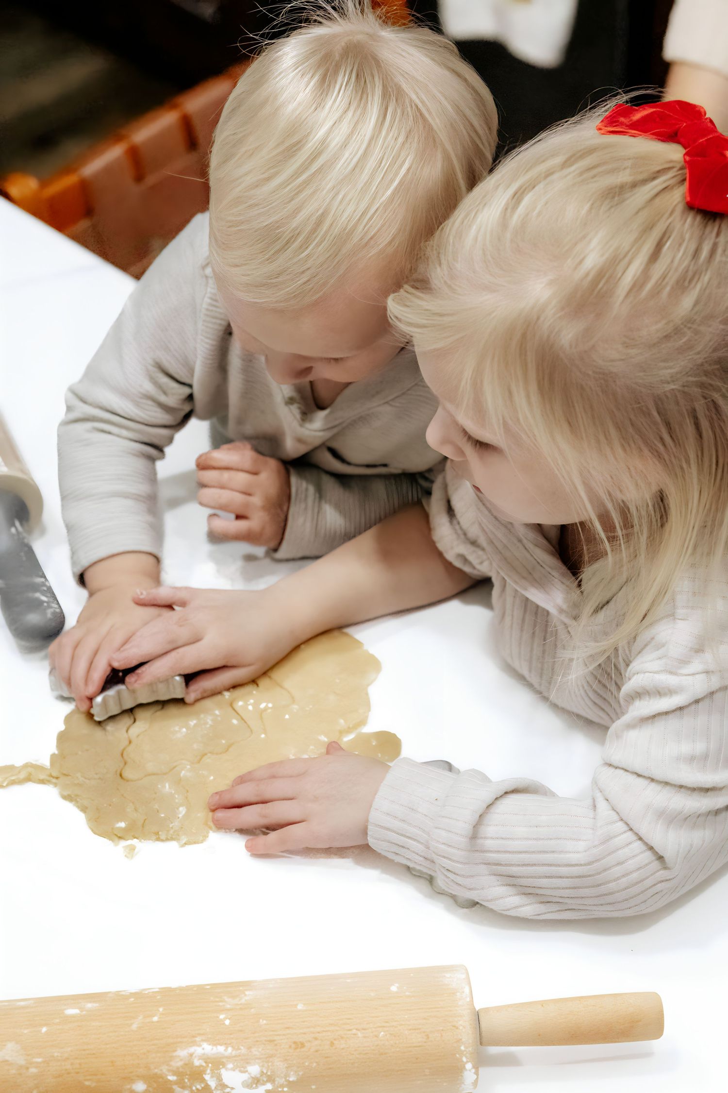Children rolling out dough together on a wooden surface.