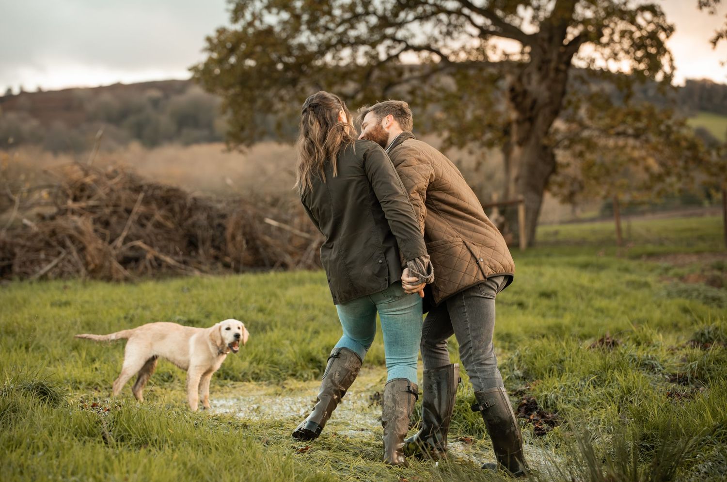 Two people and a dog walk through a grassy meadow at sunset while training outdoors.
