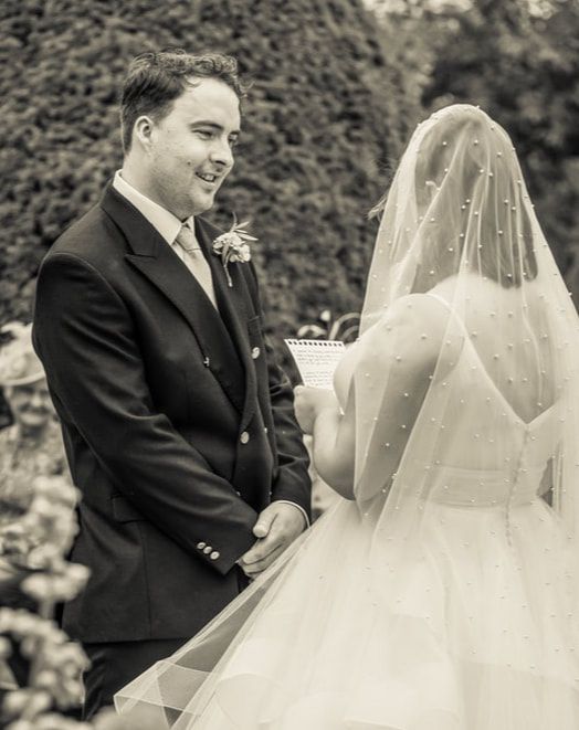 Black and white wedding photo showing a couple during their outdoor ceremony with the bride wearing a delicate beaded veil.