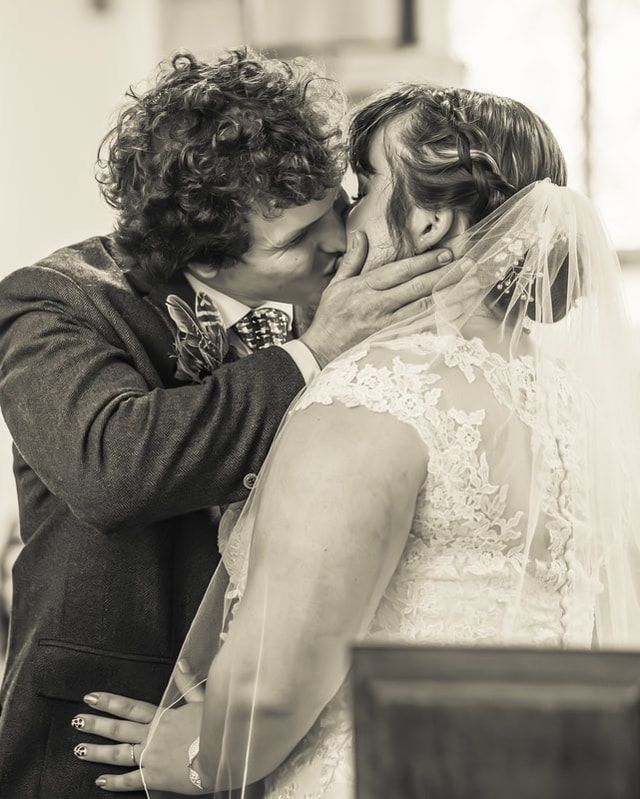 A romantic black and white wedding photo shows a tender kiss between newlyweds, with the bride wearing a delicate lace veil.
