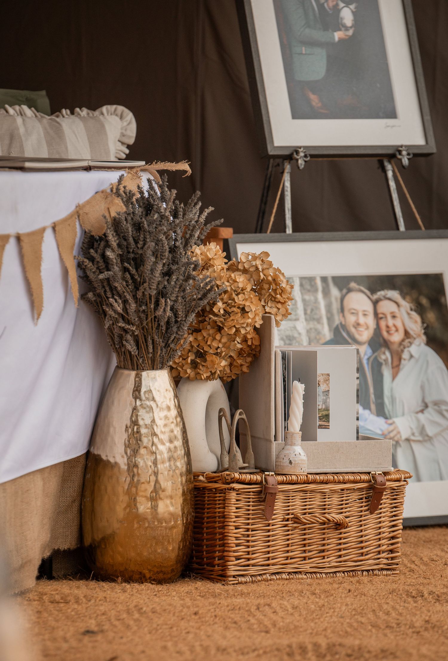 Rustic wedding display with dried lavender bouquet in ceramic vase, wicker basket, and couple photos on easel.