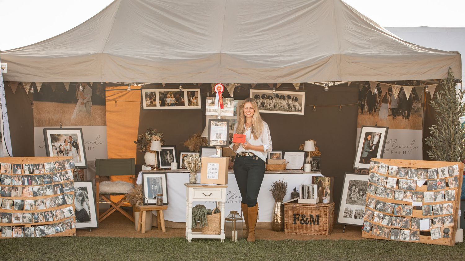 Woman standing in a decorated vendor booth displaying framed vintage photos under a tent at an outdoor market.