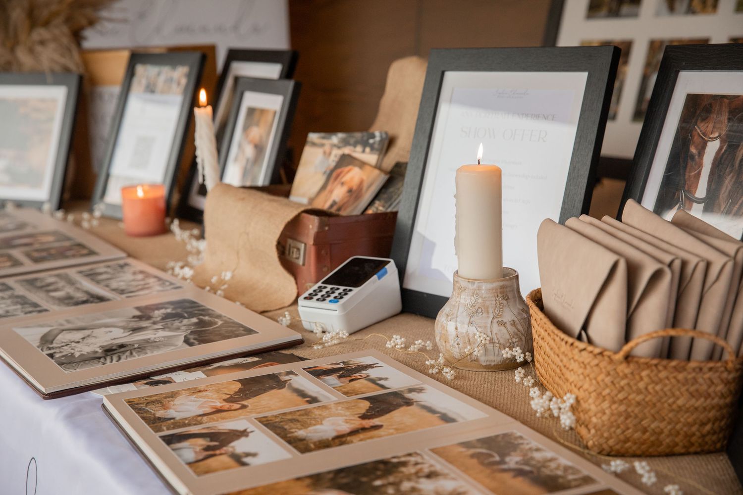 Vintage wedding memory table with framed photos, lit candles, wicker basket, and scattered dried flowers on display.