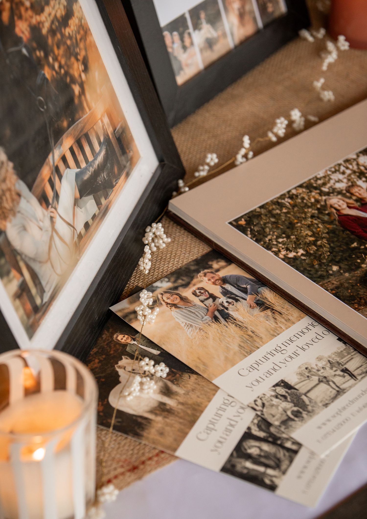 Wedding display table with framed photos, baby's breath flowers, candles, and congratulations cards on burlap runner.