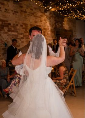 A bride in a flowing white ballgown twirls on the dance floor during a wedding reception with twinkling lights above.